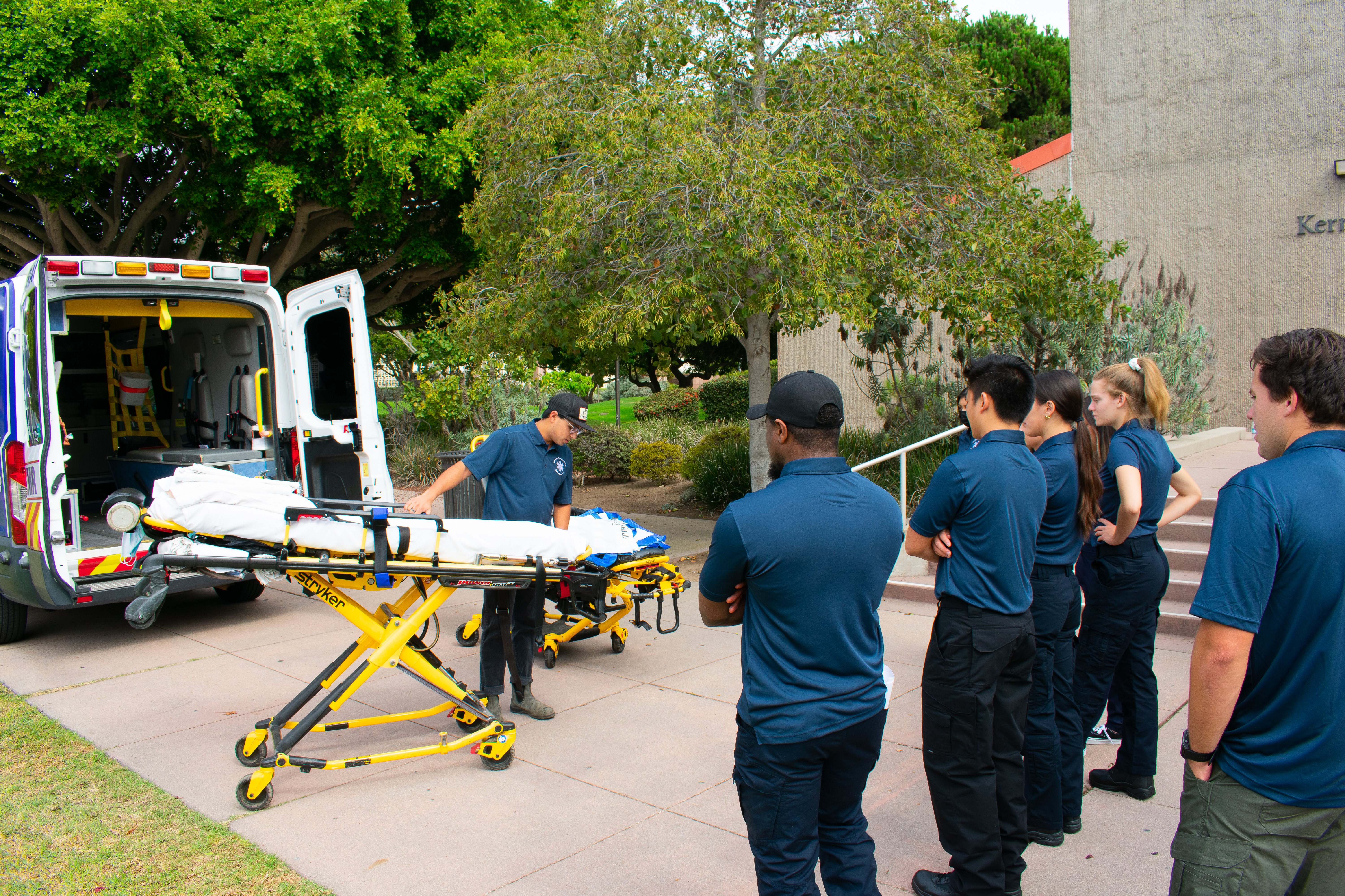 EMT Instructor showing the gurney in front of an ambulance vehicle to a handful of EMT students
